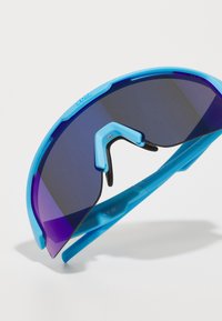 Sportsolglasögon med en livlig blå plastram, böjda linser som visar en gradation från mörklila till svart, och en funktionell justerbar bro.