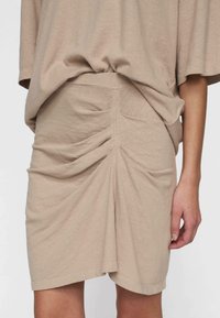 Beige knælang nederdel lavet af blødt stof, med en samlet design bagpå og en glat overflade. Kombineret med en løs top.