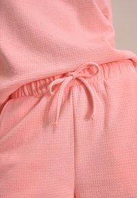 Pantalons de jogging rose clair en tissu texturé, avec taille élastique et cordon de serrage, ainsi que poches latérales. Design simple et sans couture.