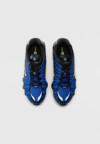 Modré a černé tenisky s texturovaným svrškem, výraznými rýhami, žlutými akcenty a gumovými úchopy na podrážce.