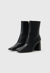 Black leather ankle boots featuring a pointed toe, a side zipper with gold hardware, and a square block heel. Smooth texture throughout.