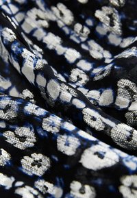 Schwarzer Stoff mit silbernem und blauen metallischen Leopardenmuster, leicht zerknittert, um Textur und Schimmer zu zeigen.