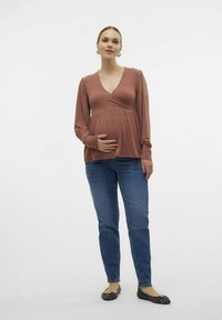 Nėštuminis viršus rusvai raudonos spalvos, supakuotas dizainas, ilgos rankovės, derinamas su mėlynomis džinsinėmis kelnėmis ir juodais butais. Lygi tekstūra, laisvas pritaikymas patogumui.