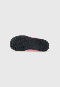 Must mustriga mustriga must tilašojo tõhusa tallaga musta kummitald, tekstuurse mustriga ja Nike swoosi logoga, mis on kinnitatud roosa spordijalatsiga, kuvatud alumisest vaatepunktist valgel taustal.