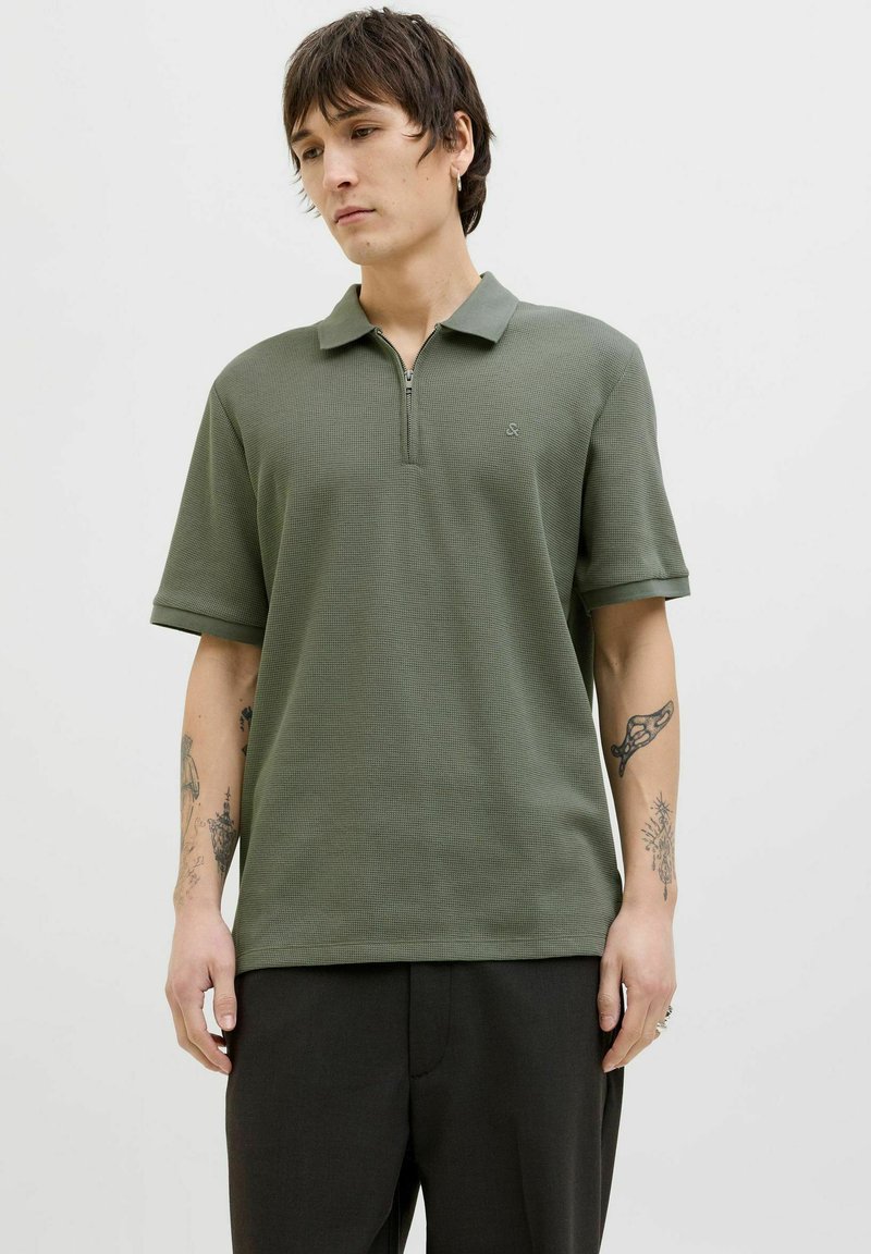 Polo shirt verde oliva con un motivo texturizzato, maniche corte e colletto con zip a metà. Presenta un piccolo logo sul petto.