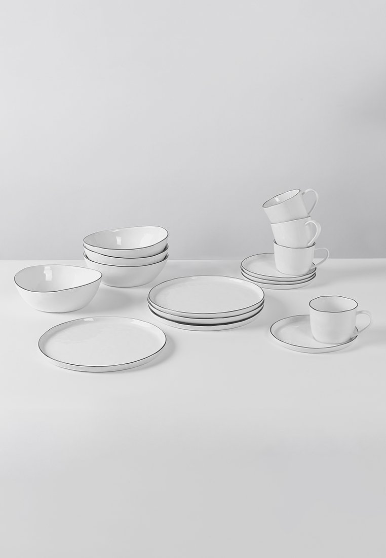 Weißes Keramikgeschirr mit minimalistischem Design, das einen dünnen schwarzen Rand aufweist. Enthält Teller, Schalen und Tassen in unterschiedlichen Größen.