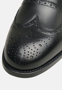 Scarpe eleganti in pelle nera, con dettagli brogue, texture liscia, punta rotonda e suola cucita. Visibili delicate perforazioni e accenti.