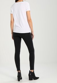 Camiseta blanca de manga corta combinada con jeans ajustados negros con detalle de cremallera en los tobillos y botas de tobillo negras con tacón.