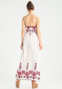 Vit maxiklänning med röd blommig broderi och justerbara spagettiband. Utsvängd design, lättviktsmaterial och smockad ryggdetalj.