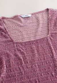 Lichtroze top met textuur en een vierkante halslijn, voorzien van een golvend patroon en zachte, gekreukelde stof. Het label vermeldt "NEXT."