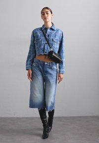 Kratka modra traper jakna z dvema žepoma na prsih, v kombinaciji z svetlomodrimi širokimi hlačami. Črna torbica čez ramo in črne škornje do kolen.