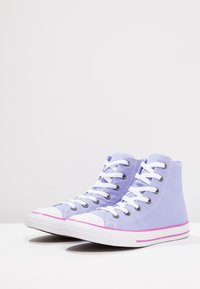 Liliowe płócienne sneakersy do kostki z białymi sznurowadłami, kontrastującym białym czubkiem i podeszwą oraz różowym akcentem wzdłuż podeszwy.