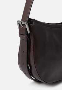 Borsa a spalla in pelle marrone con una superficie liscia, forma curva e tracolla regolabile dotata di una fibbia in metallo argentato.
