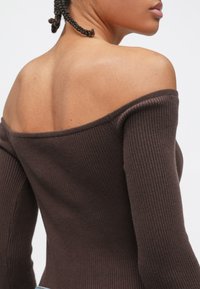 Haut marron côtelé à manches longues avec un design décolleté aux épaules. Il présente une texture douce et une silhouette ajustée, mettant en valeur le dos et la zone des épaules.