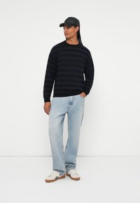 Pull marin à rayures, coupe ample, associé à un jean en denim léger. Baskets blanches avec des accents bruns. Casquette noire qui renforce le style décontracté.