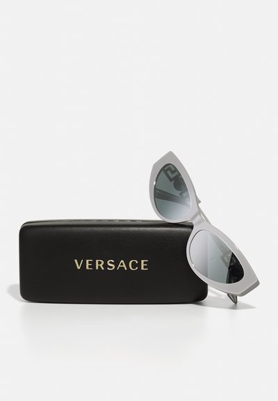 Versace-solglasögon med grå plastramar och mörkt tonade linser i en rundad kattögonform, vilande på ett svart fodral med guldtryck.