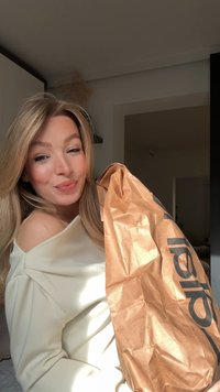 Bolsa de papel marrón con textura arrugada y logo impreso en negro, sostenida contra un fondo de tela clara y drapeada.