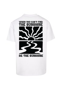Weißes T-Shirt mit fettem schwarzen Text: "WENN DU DIE SONNE NICHT FINDEN KANNST" oben, einem Grafik von Sonne und Welle, und "SEI DIE SONNE" darunter.