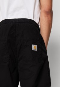 Černé cargo kalhoty s elastickým pasem, dvě zadní kapsy a malou nášivkou loga Carhartt na pravé kapse. Strukturovaná látka.