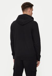 Felpa nera con cappuccio realizzata in tessuto morbido, con cappuccio strutturato, polsini e orlo a costine. Il design è casual e minimalista, privo di loghi.