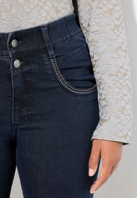 Mörka denim jeans med hög midja, med silverknappar och dekorativ sömnad på fickorna. Mjuk, slät textur.