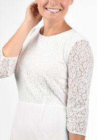 Biała koronkowa sukienka z półprzezroczystymi rękawami o długości do łokcia, okrągłym dekoltem i gładką, jednolitą spódnicą.