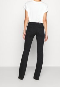 Pantalones vaqueros negros de campana con cintura alta, que cuentan con dos bolsillos traseros y un acabado liso y texturizado. Combinados con una camiseta blanca básica.