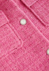 Rosa strukturiertes Gewebe mit Pailletten, zwei aufgesetzten Taschen und einem runden Knopf, der mit Kunstperlen- und Strassakzenten verziert ist.