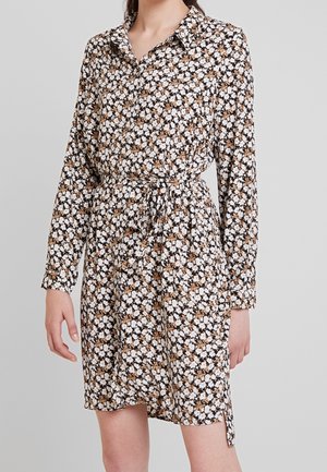 Robe chemise à fleurs avec des manches longues, un col et une taille à cordon. Le tissu présente un fond noir avec des fleurs blanches et brunes.