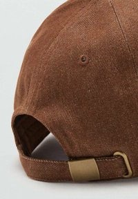 Cappellino marrone in tessuto strutturato con visiera curva, dotato di fibbia metallica sulla cinghia regolabile e foro di ventilazione cucito.