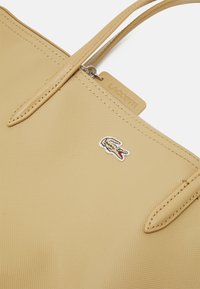 Bežna torba od teksturiranog materijala s dva drška, sa malim Lacoste logotipom i oznakom na zatvaraču.
