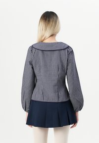Blusa a scacchi blu navy e bianca con maniche a sbuffo e colletto rotondo, abbinata a una gonna plissettata blu navy; tessuto dalla texture morbida.