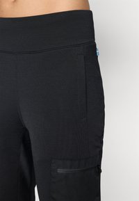 Close-up van zwarte broek met hoge taille, zijzak en klein Zweeds vlaggetje op de heup.