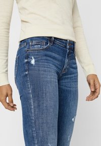 Blå denimjeans med slim fit, med slitna detaljer och midja i normal höjd. Tygstrukturen har subtila blekningar.