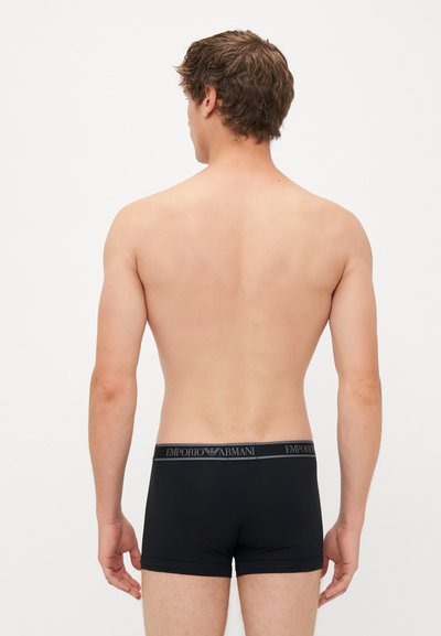 Schwarze Boxershorts mit einem breiten elastischen Bund, der mit dem Emporio Armani-Logo versehen ist, von hinten auf einem neutralen Hintergrund zu sehen.