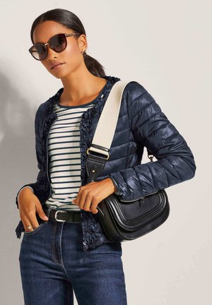 Marineblauwe pufferjas met bloemendetails, gestreept shirt, donkere spijkerbroek, zwarte handtas en oversized zonnebril, accessorized voor een casual look.