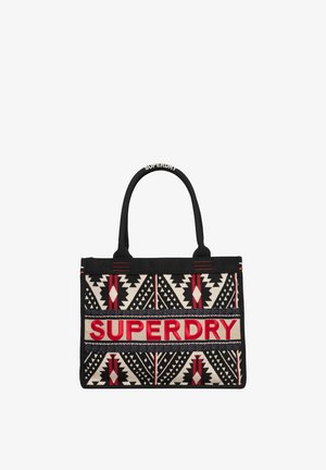 Canvas boodschappentas met zwart, rood en crèmekleurige geometrische patronen. Grote "SUPERDRY"-logo in rood met dubbele zwarte handvatten.