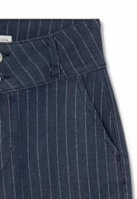 Pantalones a rayas marinos con tejido de mezclilla texturizado, que presentan un cierre de botón, pasadores para cinturón y bolsillos laterales.