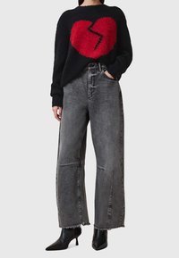 Czarny sweter z czerwonym wzorem złamanego serca, w połączeniu z szarymi jeansami z wysokim stanem, z postrzępionymi nogawkami i szerokimi nogami. Czarne botki za kostkę.