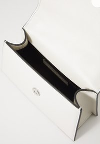 White leather handbag with a black trim. Magnetic snap closure, smooth texture, and minimalistic design. Interior shows an open compartment.