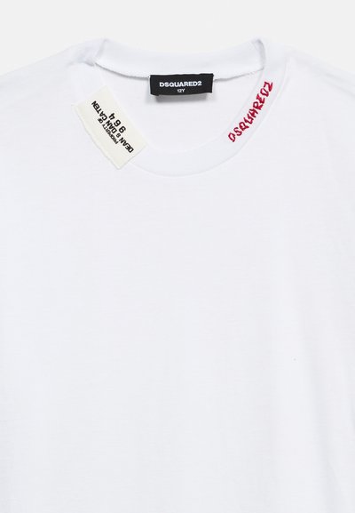 Λευκό μπλουζάκι DSQUARED2 με μαύρη ετικέτα μεγέθους 12Y, ετικέτα φροντίδας υφάσματος και κόκκινο κείμενο DSQUARED2 τυπωμένο κοντά στον στρογγυλό λαιμό.