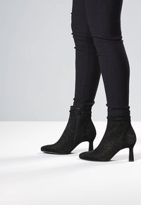 Mustat nilkkurit, joissa on teksturoitu pinta, vetoketjusuljenta, terävä kärki ja ohut korko. Materiaalina mokka ja verkko.