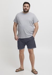 Grå bomull t-skjorte med korte ermer, paret med marineblå shorts med rullet kant, iført brune sandaler. Enkel og uformell stil.