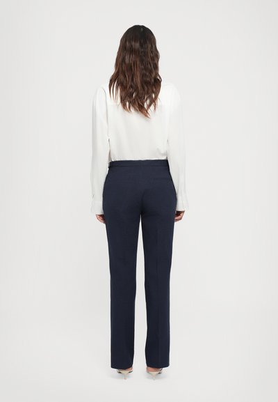Pantalons sur mesure bleu marine à jambe droite, présentant une texture subtile et une taille classique, assortis à un chemisier blanc.