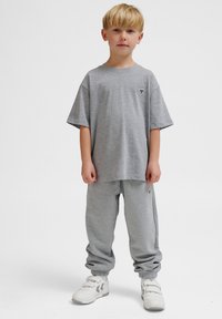 Graues Baumwoll-T-Shirt mit kurzen Ärmeln, passende graue Jogginghose und weiße Sneakers mit Riemen; einfaches Design, keine sichtbaren Muster oder Grafiken.