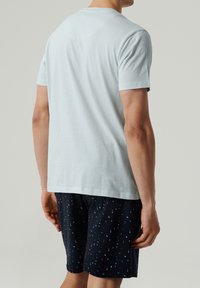 Jasnoniebieska bawełniana koszulka z krótkim rękawem, widoczna z tyłu, połączona z granatowymi szortami z przypadkowym jasnoniebieskim wzorem.