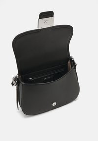 Sac à main en cuir noir avec un rabat arrondi, quincaillerie en argent et fermeture à bouton-pression centrale. L'intérieur comprend une poche zippée et une étiquette de marque.