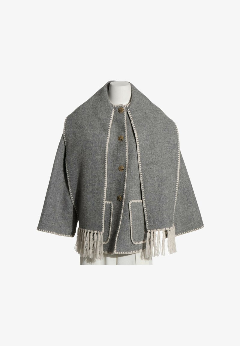 Cape en laine grise avec grand col, surpiqûres crème le long des bords, boutons en bois, poches avant et ourlet à franges, présentée sur un mannequin blanc.