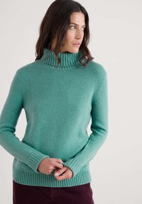 Tirkizni džemper s rol kalotom napravljen od mekog pletenog materijala. Ima rebrasti okovratnik i manžetne, s prilagođenim dizajnom i teksturiranom završnom obradom.