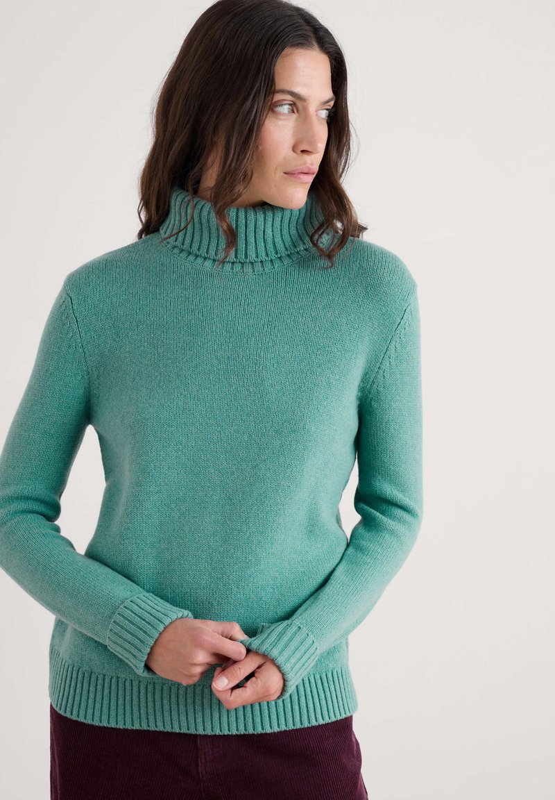 Tirkizni džemper s rol kalotom napravljen od mekog pletenog materijala. Ima rebrasti okovratnik i manžetne, s prilagođenim dizajnom i teksturiranom završnom obradom.